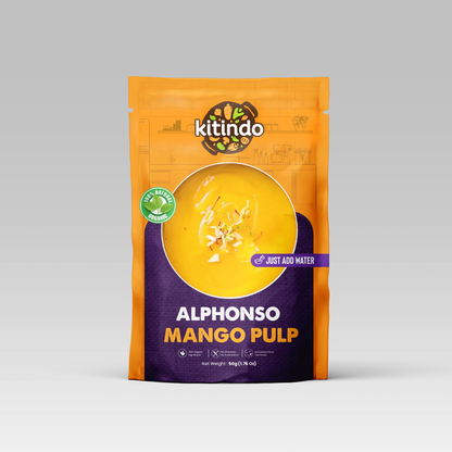 Kitindo Alphonso Mango Pulp pouch in orange and dark purple packaging, featuring a clear window showing yellow mango pulp inside, on a light gray background.